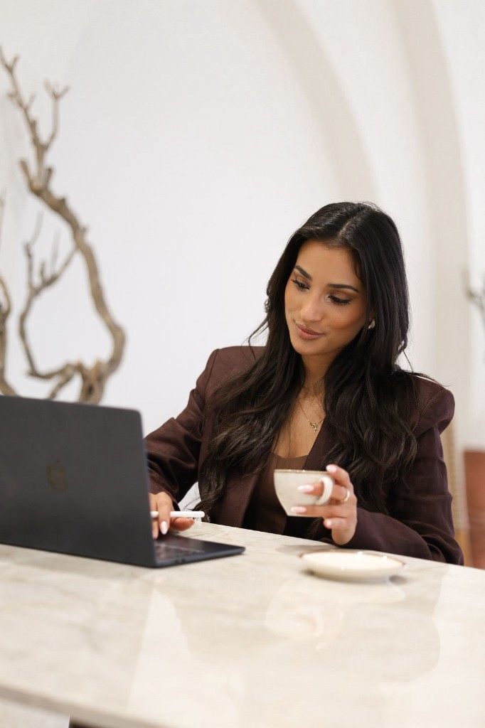Ninevah Alkan achter een laptop met een kop koffie aan een marmeren tafel