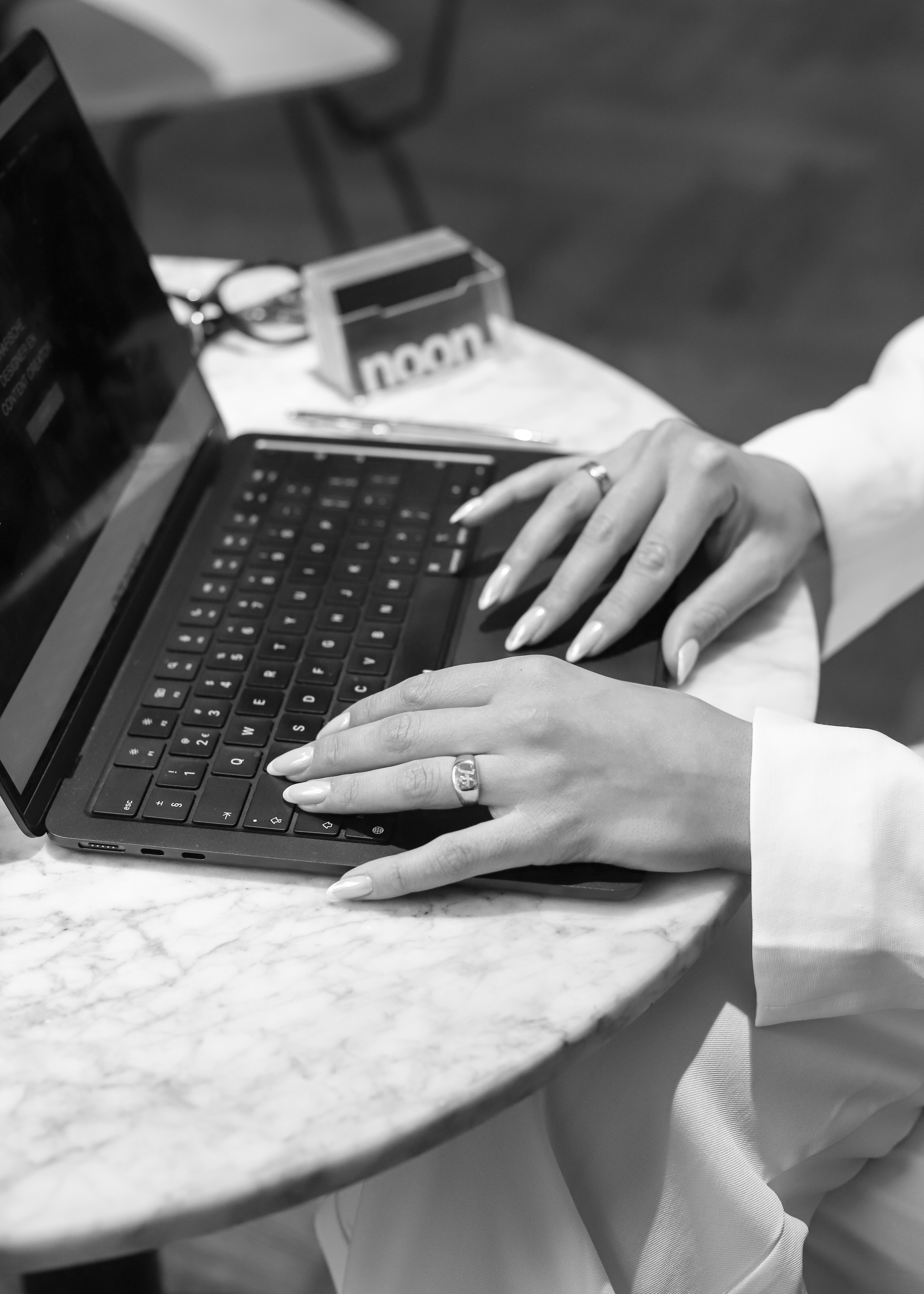 Handen op een laptop met een kaartje van Noon op een marmeren tafel