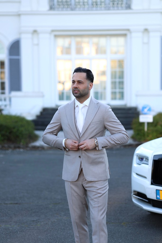 Man in beige pak naast Rolls-Royce